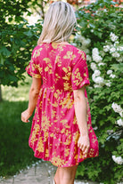 Back view of a vibrant pink floral Twirl Company dress with batwing sleeves in a garden setting.