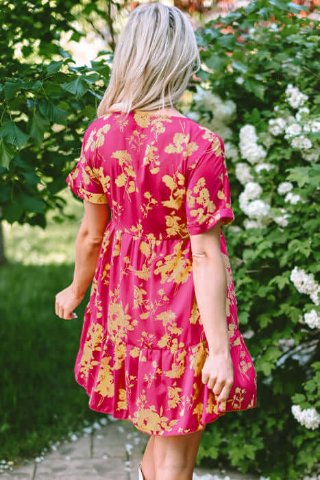 Back view of a vibrant pink floral Twirl Company dress with batwing sleeves in a garden setting.