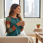 HIGHLAND RETREAT TOP worn by a woman holding a mug while seated on a couch with city views.