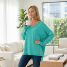 Woman wearing COZY CONCEPTS RIBBED TOP (turquoise) while enjoying coffee in a bright living room.