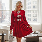 SPARKLE SEASON VELVET DRESS (Holiday Red) worn by a model, showcasing rhinestone bow accents in a festive setting.