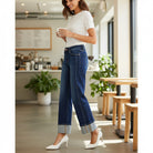 Model wearing CHARLEIGH JEANS by Risen in a cafe, showcasing dark wash cuffed wide leg silhouette.