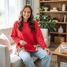 SWEETHEART BOW TOP (red) featuring floral bows, relaxed fit, and bracelet-length sleeves, modeled in a cozy indoor setting.