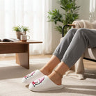 HUGS & HEARTS SLIPPERS worn with cozy pants, showcasing plush white sherpa and adorable embroidered design.