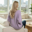 Woman wearing the SOFT HORIZONS CREWNECK in lavender, sitting on a sofa with a city view.