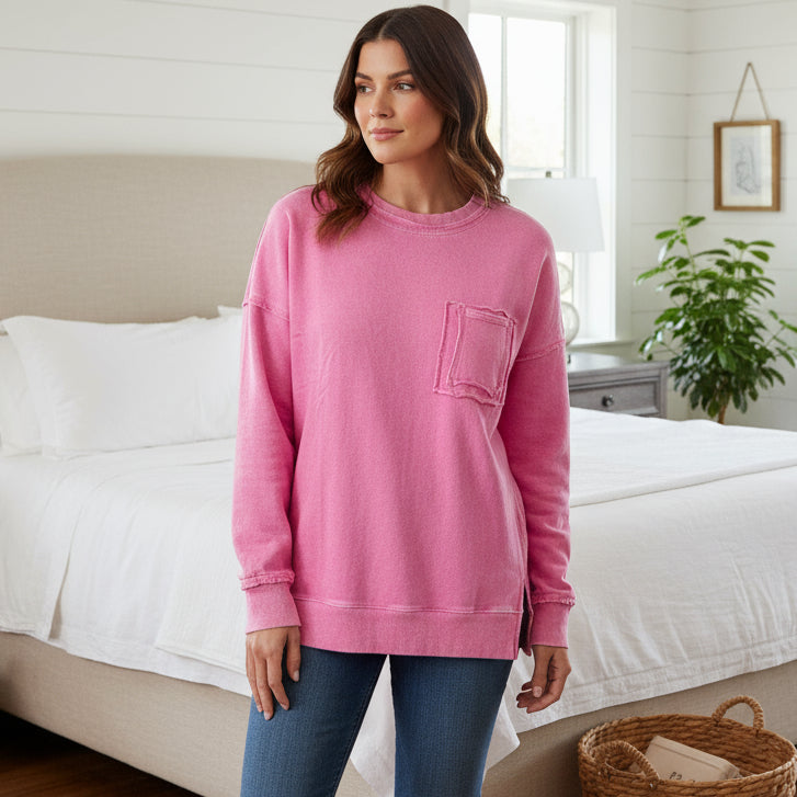Woman wearing a pink CLOUD NINE CREW pullover with a pocket, styled in a cozy bedroom.