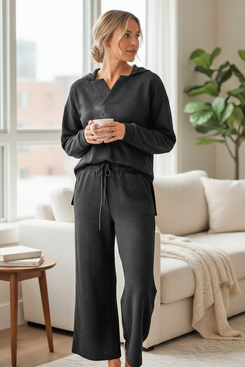 Woman in CALM & COLLECTED 2 PIECE SET, black textured lounge wear with a cozy vibe, holding a mug in modern living room.