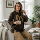 Woman wearing LOVE UNTAMED TOP - Easel, a comfy leopard patch top, holding a coffee mug in a cozy living room.