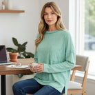 Woman sitting at a table wearing the RELAX MODE TOP (sea green) with a casual and stylish look.