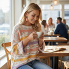A woman wearing an EASY LIKE SUNDAY SWEATER enjoys coffee in a cozy café setting.