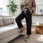 Woman in cozy sweater wearing COMFORT CULTURE PANTS (BLACK) with leopard drawstring, holding a mug.