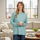 A model wearing the RELAX MODE TOP (light teal) while enjoying a cup of coffee in a cozy living room.