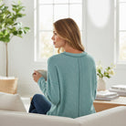 Woman enjoying tea in a light teal RELAX MODE TOP, seated on a couch in a bright living room.