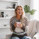 Model wearing URBAN SAFARI TOP with leopard print and color block details, smiling while holding a coffee mug.