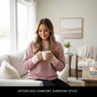 Model wearing LAZY DAY LEOPARD CREWNECK pink leopard print sweatshirt, holding a coffee mug in a cozy living room.