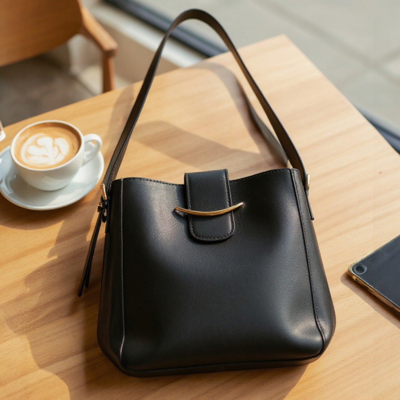 Polished Path Handbag (black) on a wooden table next to a coffee cup, showcasing its sleek design and vegan leather construction.