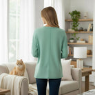 Back view of a woman wearing the RELAX MODE TOP (sea green) in a cozy living room with a cat.