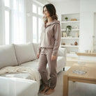 Woman wearing QUIET LUXURY SET (taupe), a zip-collar top and jogger pants, standing in a stylish living room.