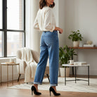 Woman wearing DARCY JEANS by Risen, showing relaxed wide-leg fit and cuffed hem in a stylish living room.