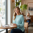 Woman in a light teal RELAX MODE TOP enjoying coffee at a cafe, showcasing casual style and comfort.