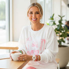 Cheerful woman in Softly Tied Crewneck with bowknot pattern, enjoying coffee in bright cafe setting.