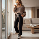 Woman enjoying coffee in cozy outfit, wearing COMFORT CULTURE PANTS (BLACK) with leopard drawstring.