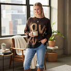 LOVE UNTAMED TOP - Easel worn by a model, showcasing the leopard patch letters and cozy design with a cup in hand.
