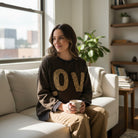 LOVE UNTAMED TOP - Easel worn by a woman in a cozy living room, showcasing its leopard patch letters and comfy style.