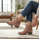 Woman wearing VERY G CAROLINA ANKLE BOOT in rose tan suede, styled with denim jeans in a cozy living room.