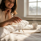 Woman holding the LOVE STORY Earrings and Necklace Set (gold) in bed with coffee and a book.