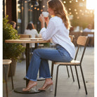 Woman enjoying coffee while wearing FAE JEANS by Risen, styled with a casual white shirt and clear heels.