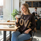 LOVE UNTAMED TOP - Easel styled in a cozy cafe, showcasing leopard patch letters and a relaxed look.