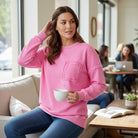 Woman wearing a pink Cloud Nine Crew pullover while enjoying a coffee in a cozy café setting.