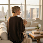 Woman wearing LOVE UNTAMED TOP - Easel, enjoying a cozy moment in a modern living room with city view.