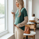 Woman wearing EVERYDAY BALANCE TOP in jade colorblock while holding a cup in a cozy café setting.