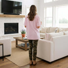 Woman wearing LULU MAC MOSSY OAK - COMFORT COLORS TEE (pink) with camo leggings in cozy living room.