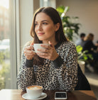 A woman enjoying her coffee wearing THE PERFECT SPOT Ribbed Top in snow leopard print, showcasing effortless style.