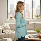 Woman wearing RELAX MODE TOP (light teal) in a cozy living room, showcasing its relaxed fit and soft fabric.