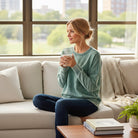 Woman wearing SKYLINE CREW (Dusty Teal) pullover while enjoying a cozy moment on the couch.
