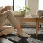 A woman enjoys coffee while wearing HAZEL SLIP-ON MULES, showcasing the stylish knotted strap and stacked block heel.