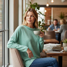 RELAX MODE TOP (sea green) worn by a woman in a cozy café, showcasing its soft melange fabric and relaxed style.