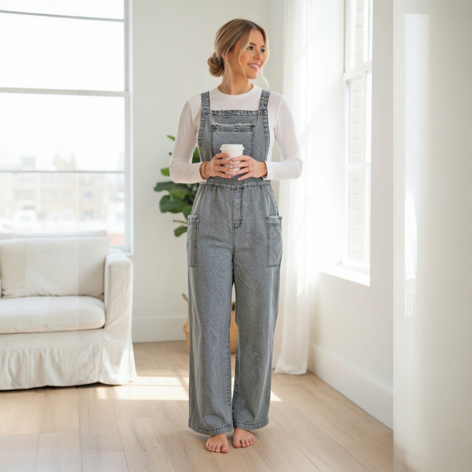 DENIM 4 DAYS OVERALLS - BIBI worn by a woman in a relaxed fit, enjoying a cozy indoor setting with a drink.