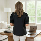 Back view of a woman wearing the STRUCTURED GRACE TOP, a tailored black blouse with puff sleeves.