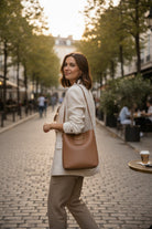 Stylish woman carrying a POLISHED PATH HANDBAG (cinnamon) in a chic street setting.