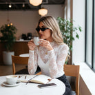 FLORAL FROST MESH TOP worn by a woman in sunglasses, sipping coffee at a cafe, showcasing a stylish and elegant look.