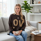 Model wearing LOVE UNTAMED TOP - Easel with leopard print letters, sitting on a couch and holding a mug.