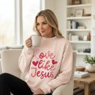 Young woman wearing LOVE LIKE JESUS PULLOVER while holding a coffee cup in a cozy living room.