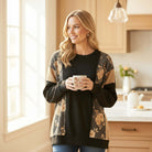 HOMETOWN HARMONY TOP - Heimish model in cozy floral color block top, enjoying a drink in a stylish kitchen.