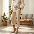 A model wearing COMFORT CULTURE PANTS (cream) with leopard drawstring, showcasing cozy fleece lining in a stylish living room.