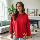 SWEETHEART BOW TOP (red) featuring a relaxed fit, floral bow patches, and bracelet-length sleeves in a stylish indoor setting.